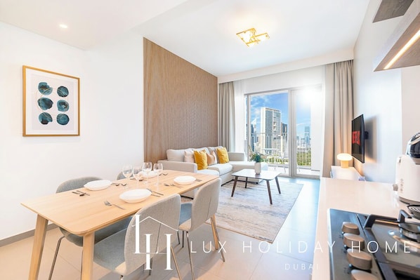 A modern hotel room with a dining area, a sofa, a TV, and a city view.