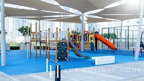 Zona de juegos al aire libre con tobogán, estructuras para escalar y asientos a la sombra.