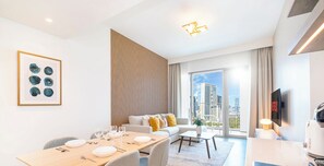 A modern hotel room with a dining area, a sofa, a TV, and a city view. - LUX The Downtown Zabeel View Suite (Dubai)