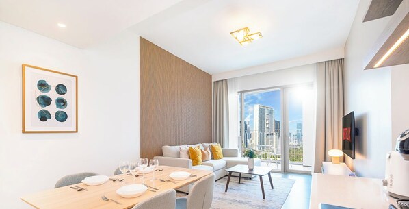 A modern hotel room with a dining area, a sofa, a TV, and a city view. - LUX The Downtown Zabeel View Suite (Dubai)