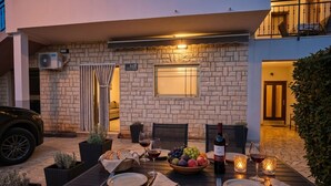 An outdoor dining area with a table set for two, a bottle of wine, fruit, and candles. - Apartment Fuzalo · Relax & BBQ by Villas Guide (Krnica)