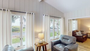 Et værelse med en lædersofa, et lille bord med en lampe og store vinduer med gardiner.