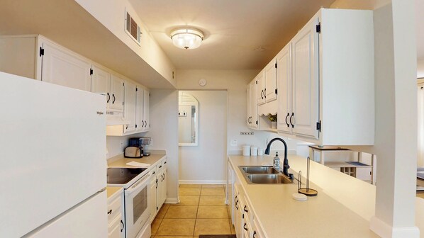 A modern kitchen with white cabinetry, a built-in oven, a sink, and a coffee maker.