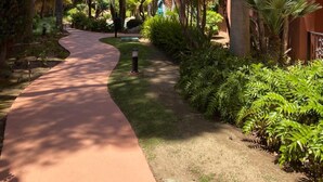 A pathway flanked by lush greenery and palm trees, leading to a building with a red facade. - Apartment 'Don Carlos Marbella Beach' with Shared Pool, Wi-Fi and Air Conditioning (Marbella)