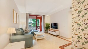 A modern living room with a sofa, coffee table, TV, and a plant. - Apartment 'Don Carlos Marbella Beach' with Shared Pool, Wi-Fi and Air Conditioning (Marbella)