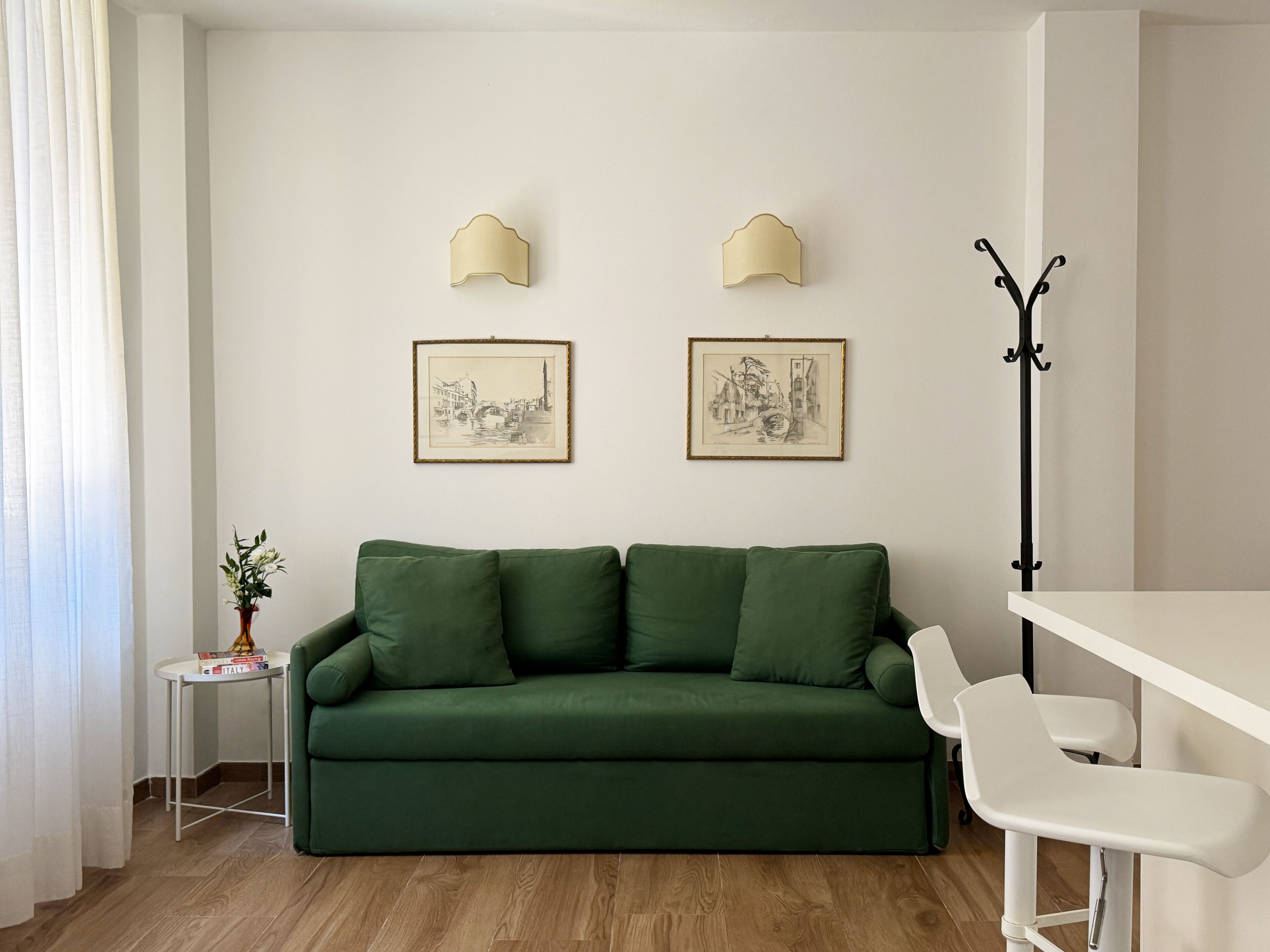 Een groene bank, een witte tafel en twee ingelijste foto's aan de muur.