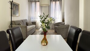Uma sala de estar moderna com uma mesa branca, poltronas de couro preto, um sofá cinza e um vaso com flores brancas.