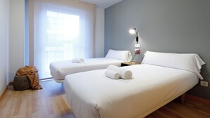 A hotel room with two beds, a large window, a bedside lamp, and a small table with a vase. - Vita Homes by Upper Luxury Housing (Santiago de Compostela)