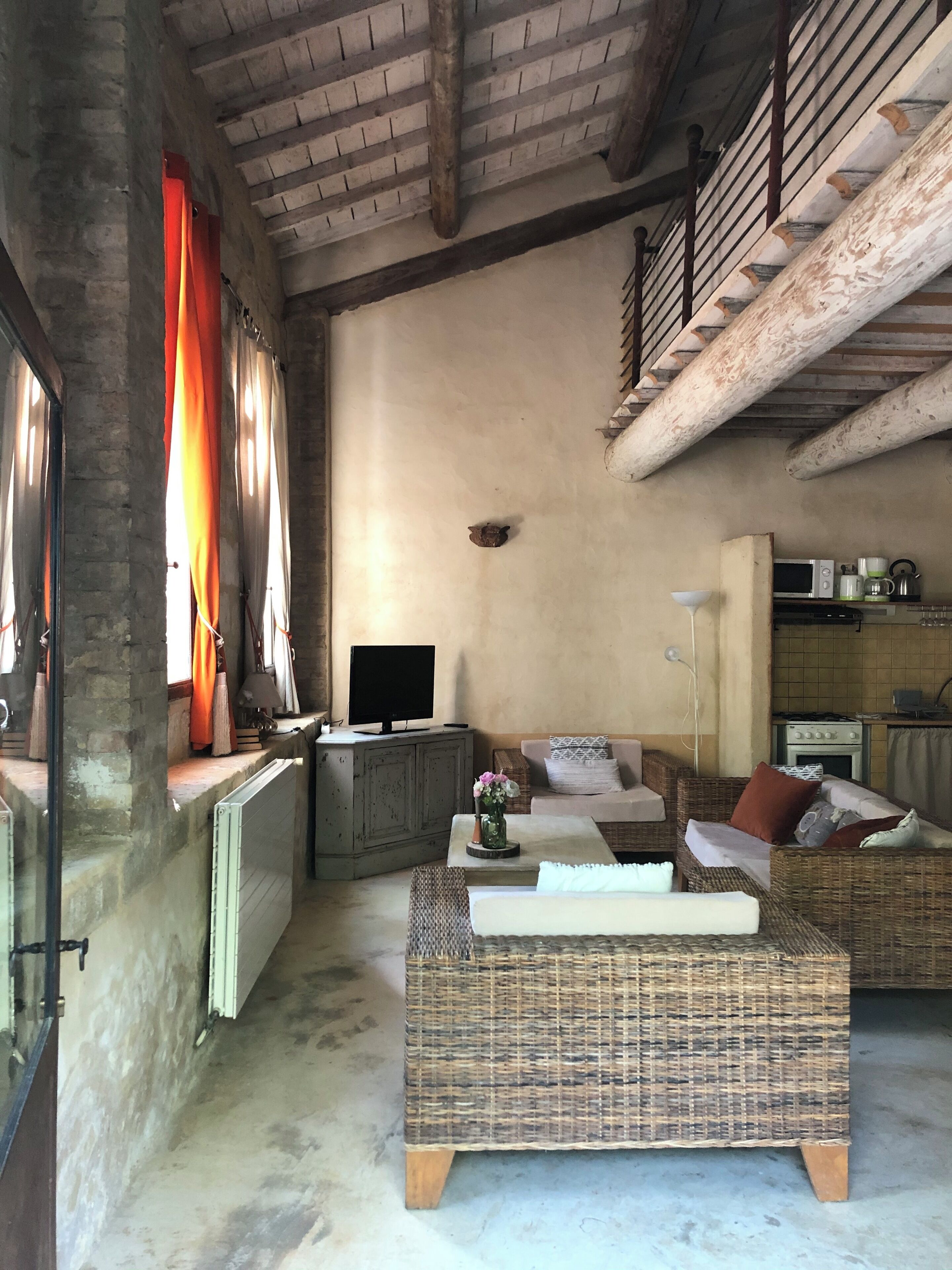 A rustic living room with a fireplace, a television, wicker furniture, and a kitchen area with appliances.