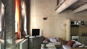Een landelijke woonkamer met een open haard, een televisie, rieten meubels en een keuken met inbouwapparatuur.