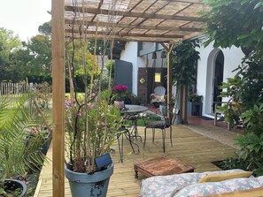 An outdoor patio with a wooden deck, a table with chairs, a sofa, and various potted plants. - Maison Zen Swimming pool Near cycle track (Andernos les Bains)