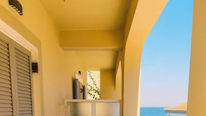 A balcony with a table set for two, chairs, a cabinet, and a view of the sea. - Beachfront Panorama Double Room in Kythira (Kithira)