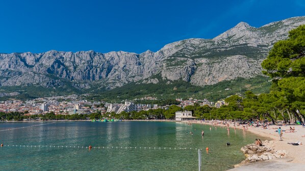 A coastal city with a clear view of mountains in the background, a beach with people, and a calm sea.