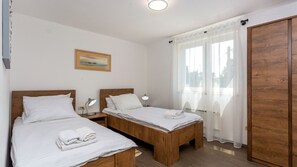 A double room with two beds, a bedside table with a lamp, a painting on the wall, and a large wooden wardrobe.