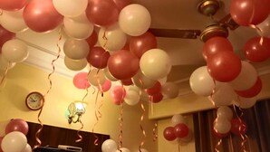 A room with a ceiling decorated with red and white balloons, a clock on the wall, and a television on a stand.