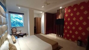 A hotel room with a large bed, a TV, a window with a view, and a red patterned wall.
