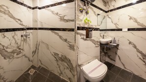 Une salle de bain avec des murs en marbre, une douche, des toilettes et un lavabo.
