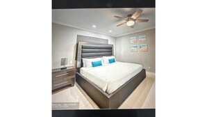 A bedroom with a bed, nightstands, a ceiling fan, and wall art. - Modern Spacious Beach Villa 1 Pompano Beach (Pompano Beach)