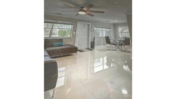 A spacious living area with a large window, a ceiling fan, and a dining table with chairs. - Modern Spacious Beach Villa 1 Pompano Beach (Pompano Beach)