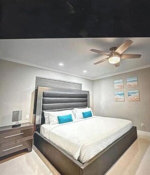 A bedroom with a bed, nightstands, a ceiling fan, and wall art. - Modern Spacious Beach Villa 1 Pompano Beach (Pompano Beach)