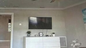 A modern living room with a flat-screen TV mounted on the wall, a white entertainment unit below, and a ceiling fan. - Modern Spacious Beach Villa 1 Pompano Beach (Pompano Beach)