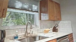 A kitchen with wooden cabinets, a stainless steel sink, and a window with a view of greenery. - Modern Spacious Beach Villa 1 Pompano Beach (Pompano Beach)