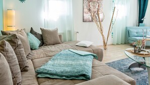 A modern living room with a beige sofa, a glass coffee table, and a blue patterned rug.