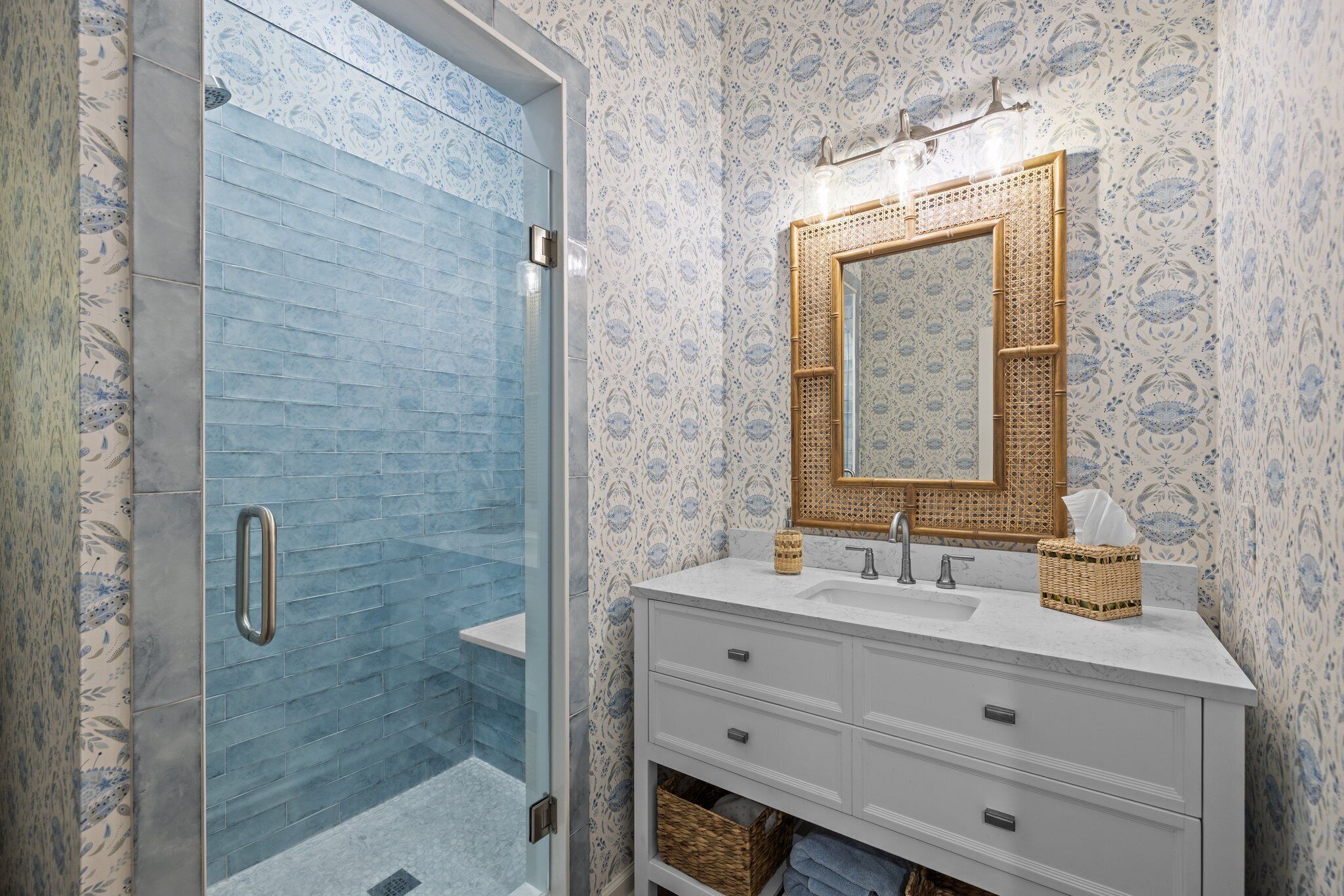 A bathroom with a glass shower enclosure, a white vanity with a mirror, and patterned wallpaper.