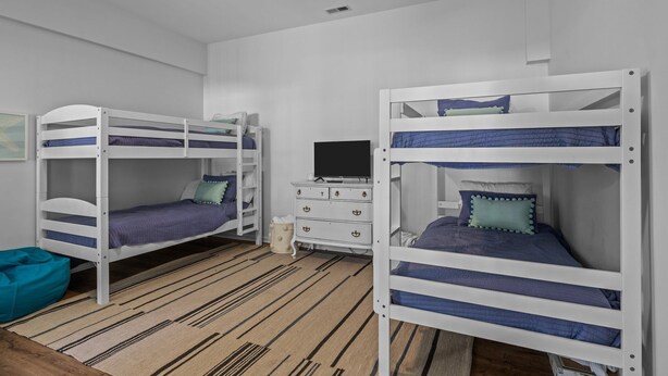 A room with bunk beds, a dresser, and a television. - Shiloh Cottage in Atlantic Beach, NC (Atlantic Beach)