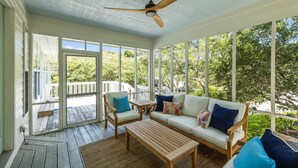 A covered porch with a ceiling fan, a wooden table, two chairs, and a sofa with cushions. - Shiloh Cottage in Atlantic Beach, NC (Atlantic Beach)