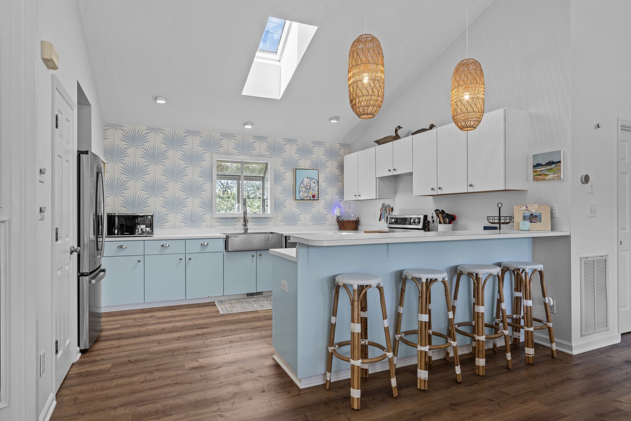 A modern kitchen with light blue cabinets, a central island with bar stools, a skylight, and pendant lighting.