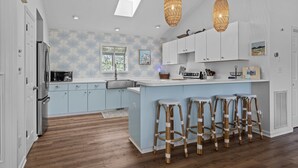 A modern kitchen with light blue cabinets, a central island with bar stools, a skylight, and pendant lighting. - Shiloh Cottage in Atlantic Beach, NC (Atlantic Beach)