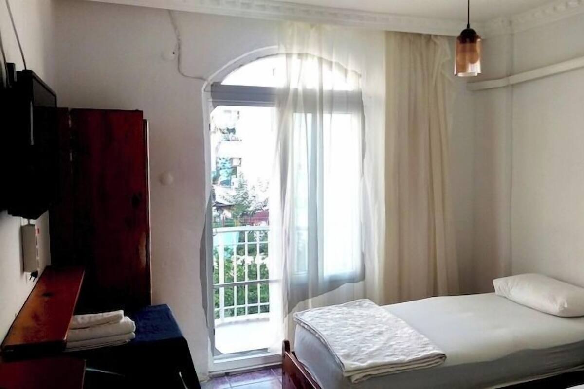 Ein Schlafzimmer mit einem Bett, einem Nachttisch aus Holz, einem Schreibtisch mit Stuhl und einem fenster mit Vorhängen.