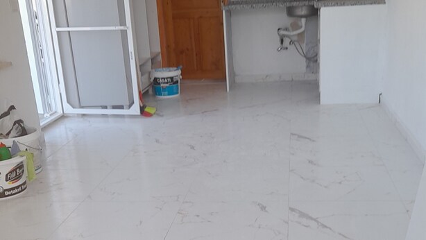 A spacious kitchen with white cabinets, a marble floor, and a wooden door. - Akasya Pansiyon & Apart (Anamur)