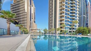 A swimming pool with lounge chairs, surrounded by high-rise buildings. - Iris Blue - Colourful One Bedroom in The Marina (Dubai Marina)
