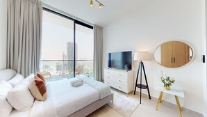 A modern hotel room with a large bed, a TV, a desk, and a view of the city.