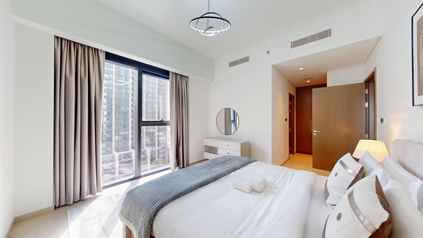 Een moderne hotelkamer met een groot bed, een nachtkastje, een spiegel en uitzicht op de stad door ramen van vloer tot plafond.