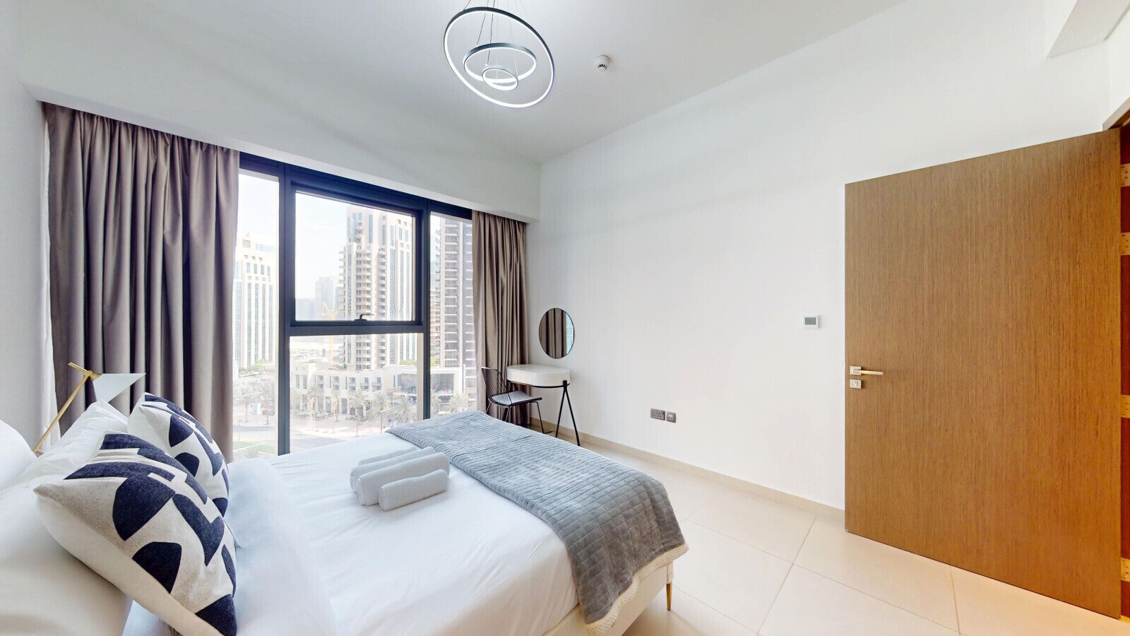 A modern hotel room with a large bed, a desk, and a view of tall buildings.