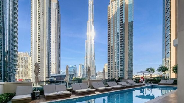 A rooftop pool area with lounge chairs and a view of tall buildings. - Vibrant 2 Bedroom l Pool with Burj Khalifa View (Downtown Dubai)