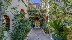 Un étroit sentier de pierre, bordé d’une végétation luxuriante et de plantes en pot, mène à un bâtiment doté de fenêtres en arc de cercle et surmonté d’une structure bleue.