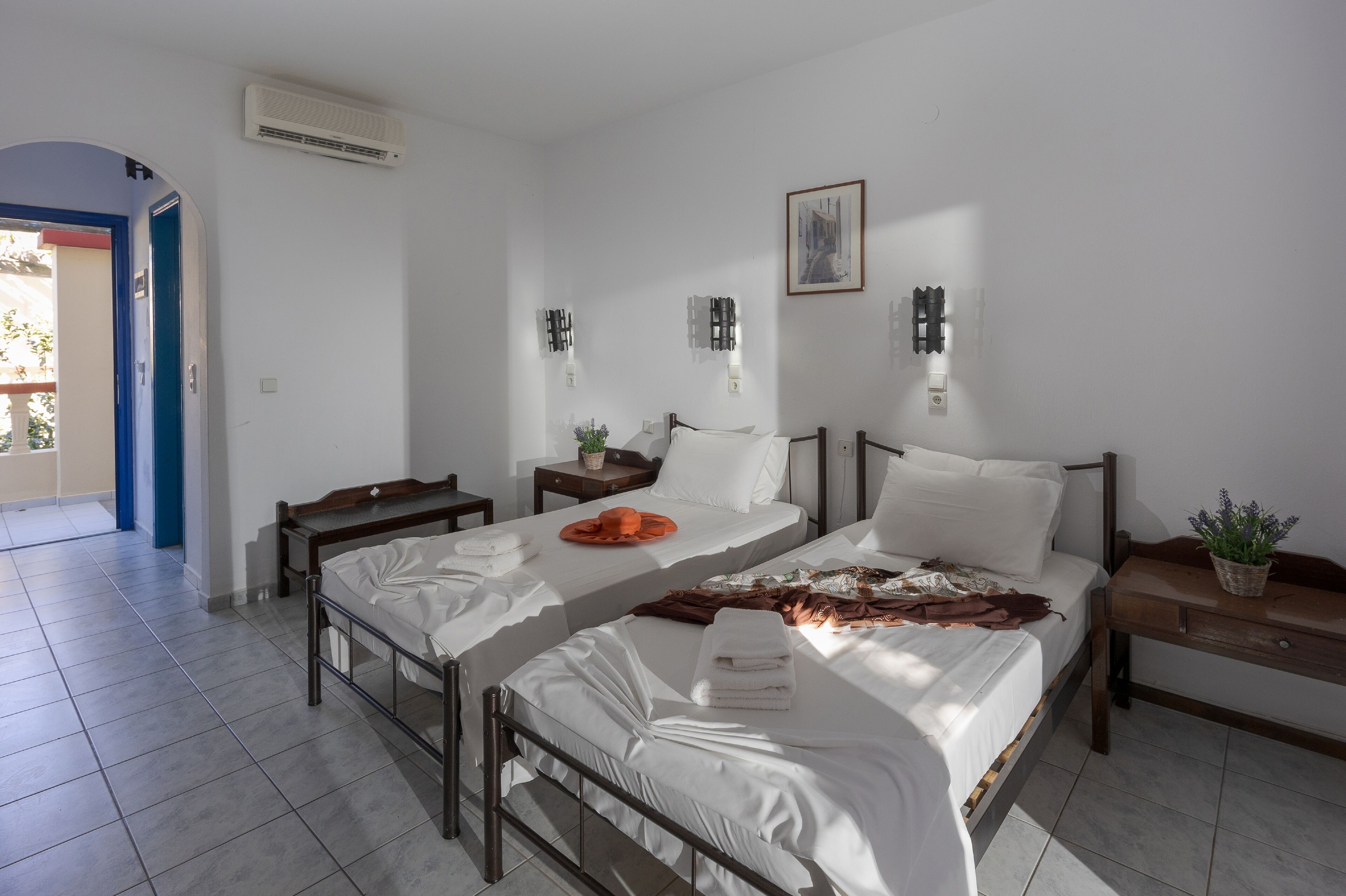 A hotel room with two beds, a small table, a nightstand, and a potted plant.