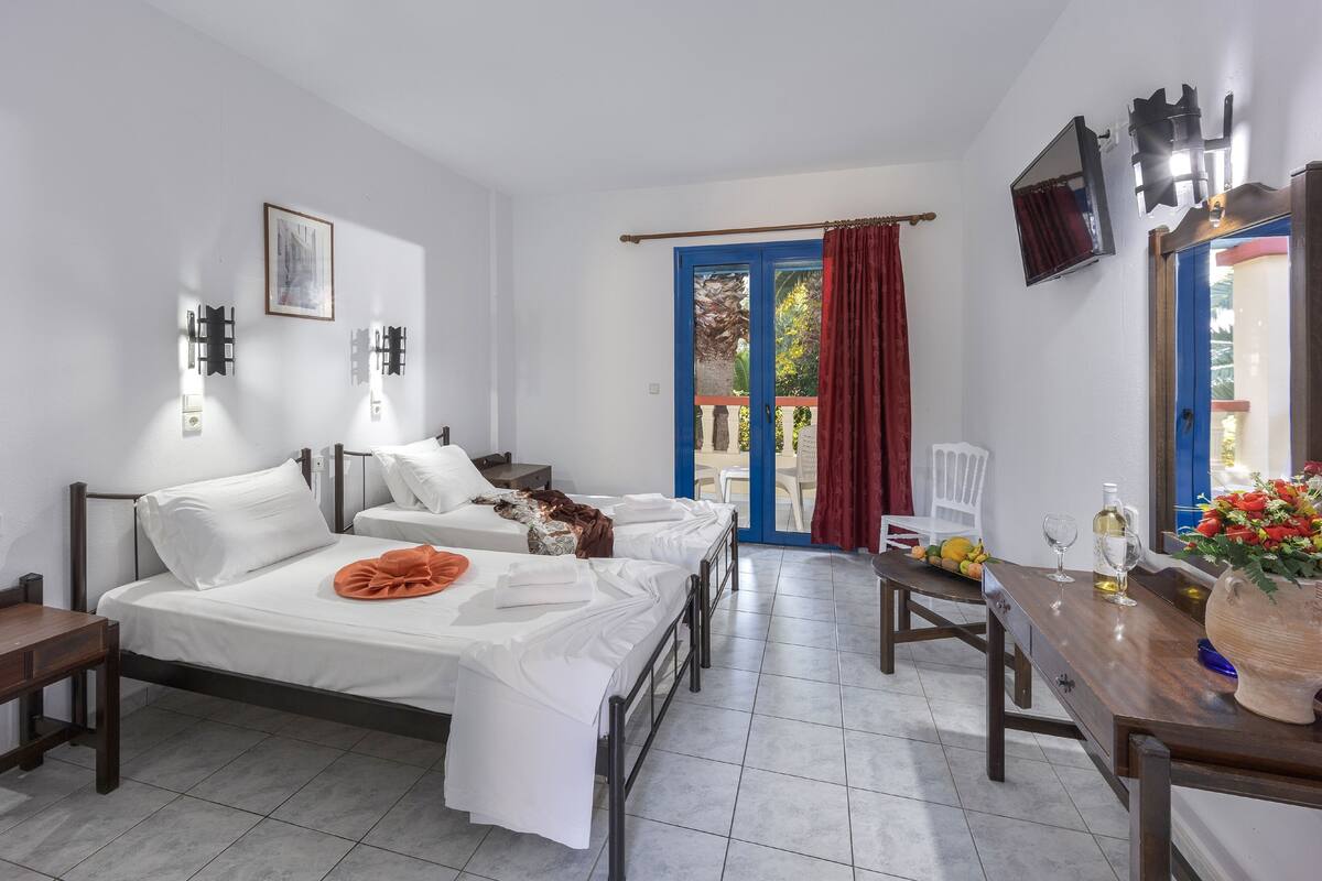 Una habitación de hotel con cama, escritorio, silla, ventana con cortinas y puerta.