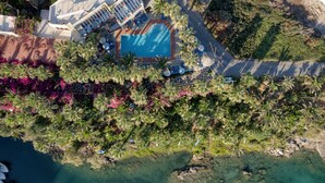 Vue aérienne d’un complexe hôtelier doté d’une piscine entourée de palmiers et d’une plage.