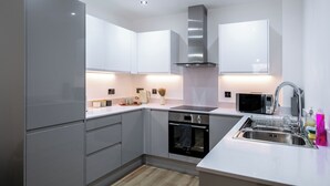 A modern kitchen with grey cabinets, a stainless steel range hood, a built-in oven, a microwave, and a sink with a faucet.
