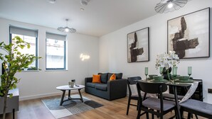 A modern living room with a grey sofa, a dining table set for four, and a large window with blinds.