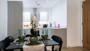 A modern dining area with a table set for four, a kitchen in the background, and a wooden door to the right.