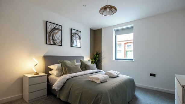 A bedroom with a bed, bedside tables, a night lamp, and two wall-mounted artworks.