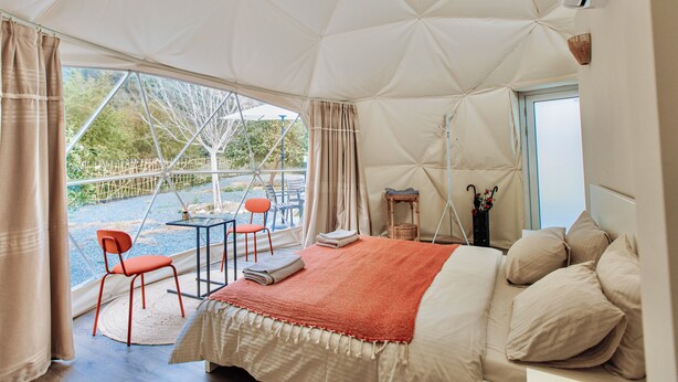 Una tenda arredata con un letto, un tavolo, due sedie e vista sull'esterno.