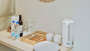 Un bancone in cucina con un dispenser d'acqua, bottiglie, bicchieri, un vassoio con utensili e una macchina da caffè.