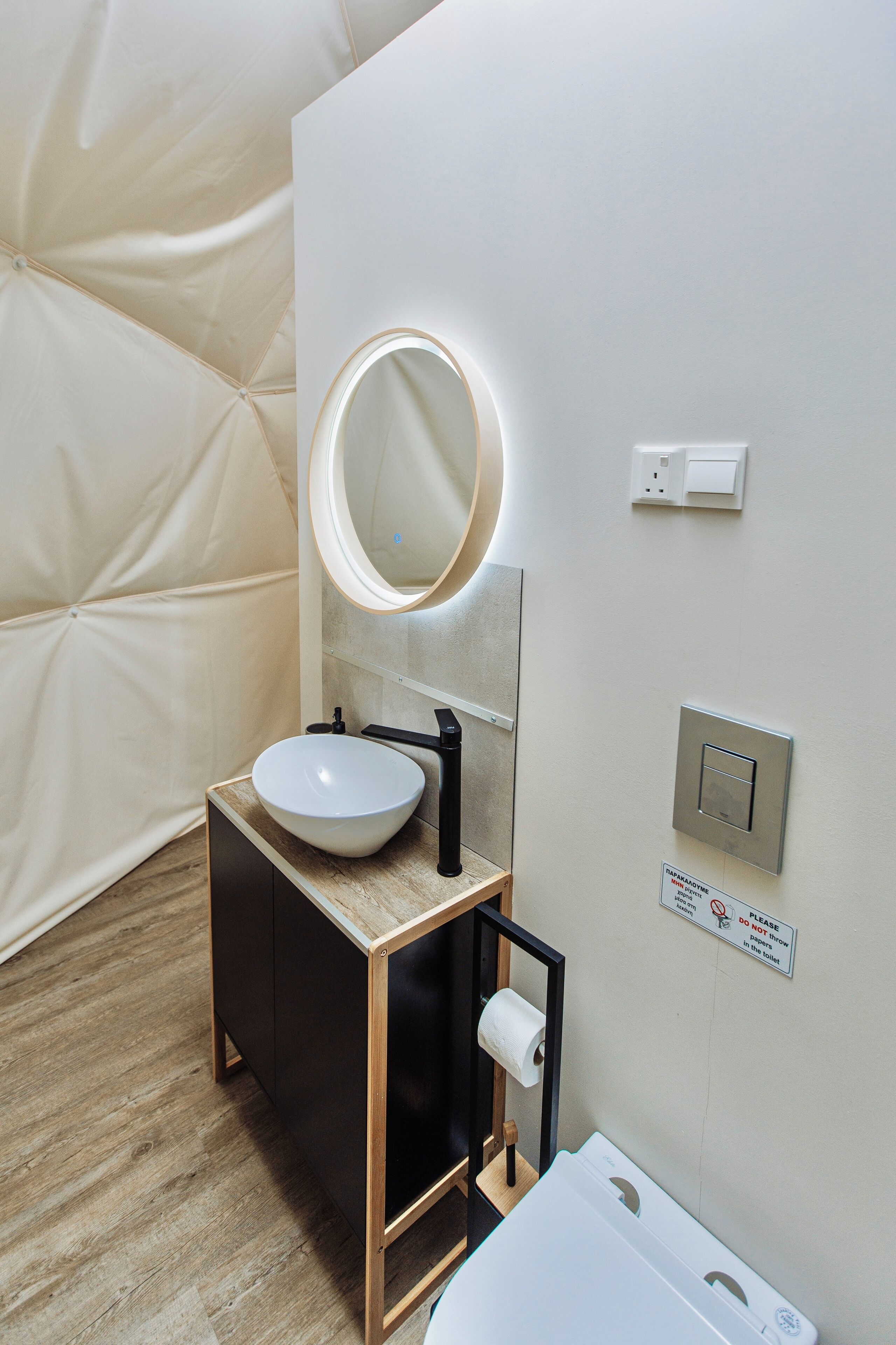 A modern bathroom with a white sink, black cabinet, and a round mirror with a light.